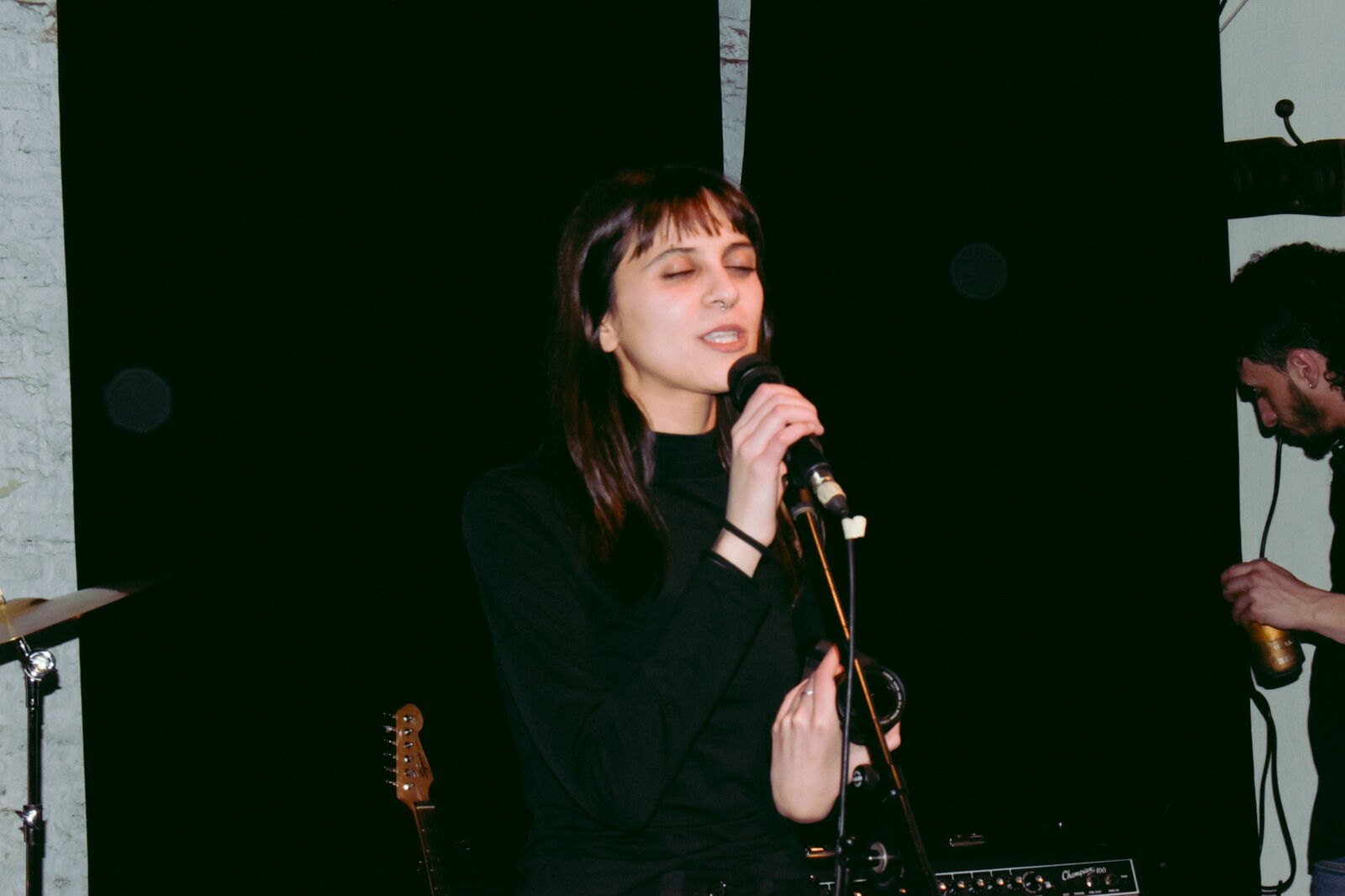 Cantante con los ojos cerrados frente al micrófono, sobre fondo negro
