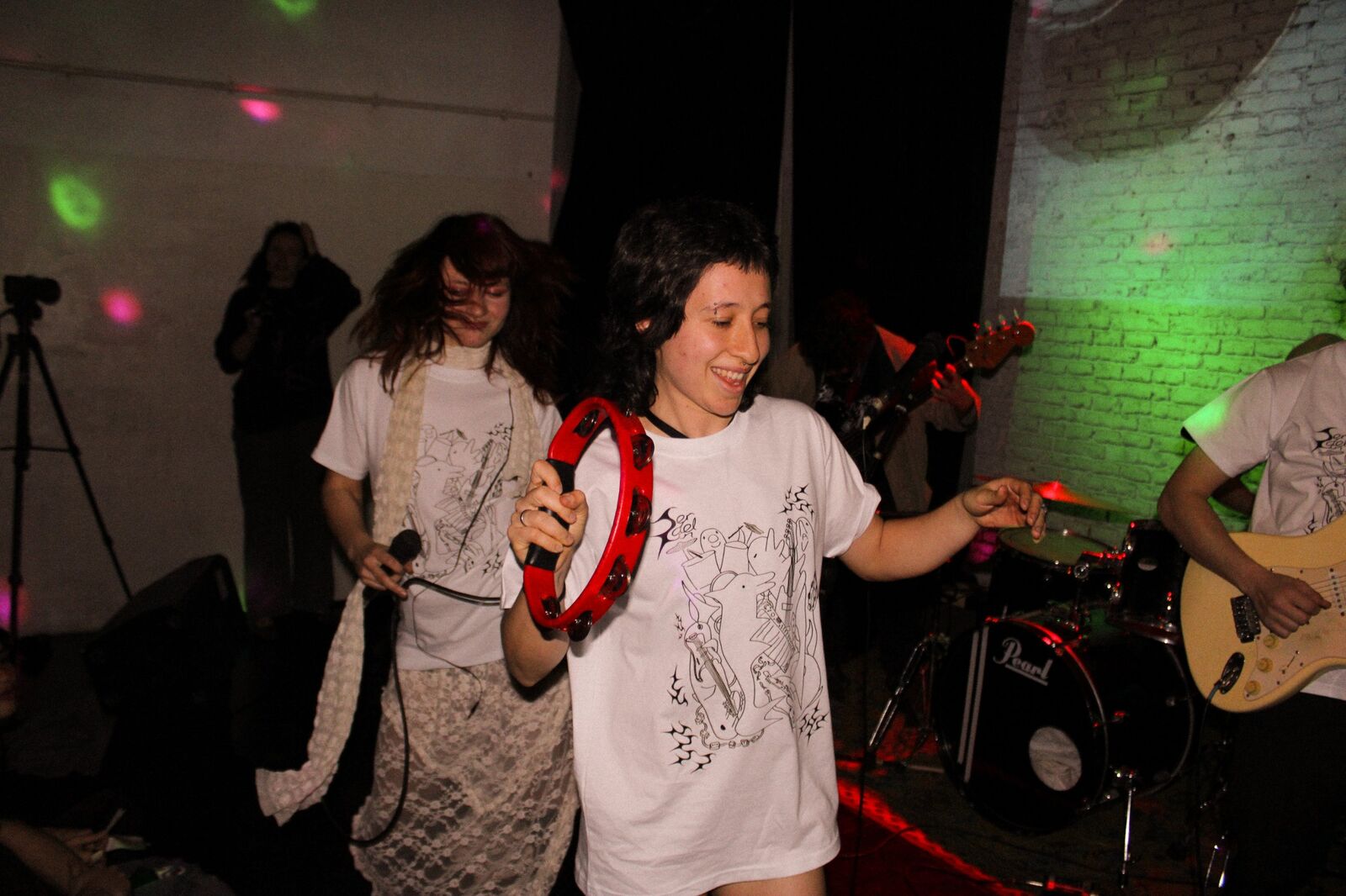 Integrante de la banda bailando con una pandereta roja, con remera blanca estampada