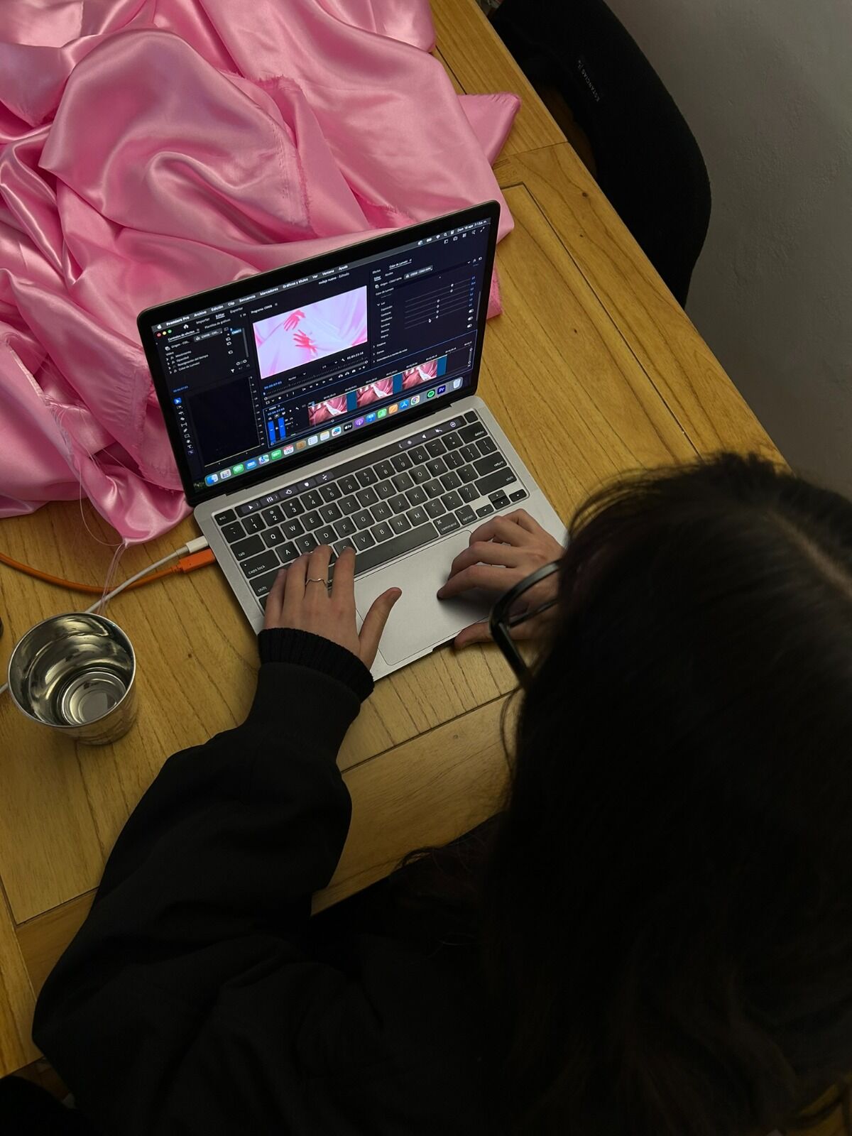 Una de las artistas edita un video rosa en la computadora, junto a una tela de satén rosa