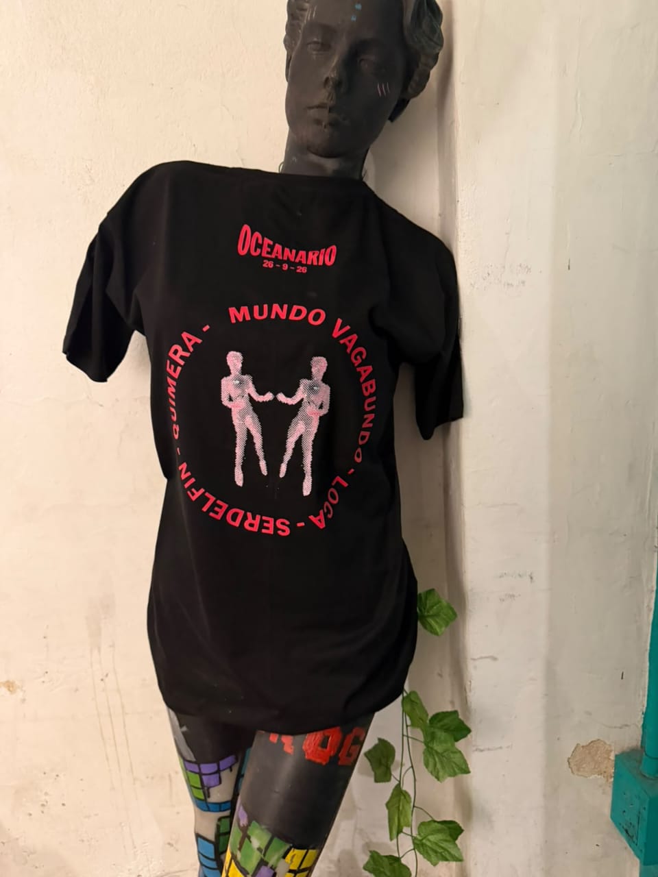 Remera negra de la fecha Oceanario en un maniquí, con estampa fucsia y los nombres de las bandas en círculo